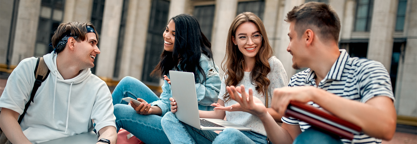 Students sitting outside a building chatting and smiling together