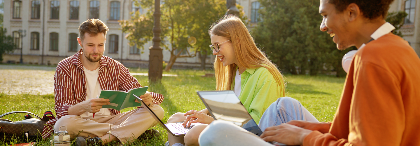 Students sat outside on grass studying and smiling