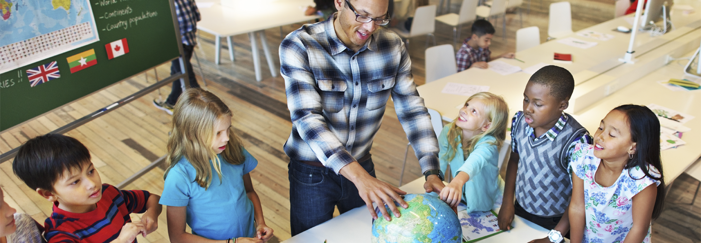 A teacher with children stood over a globe of the world, with children pointing to it