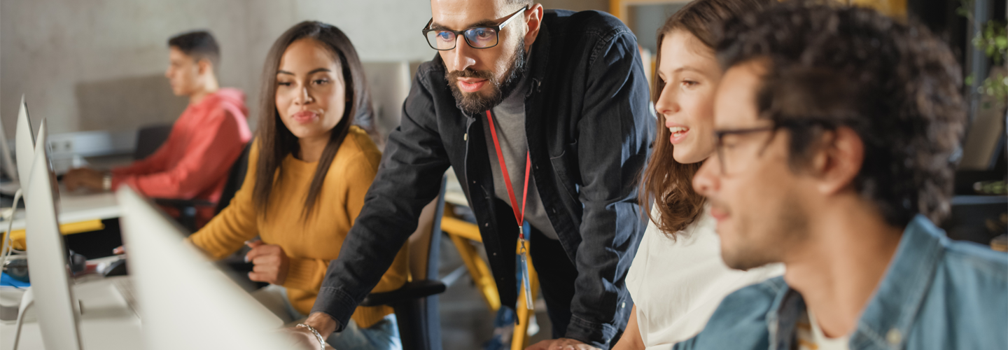 A teacher stoof over computers that students are sat at