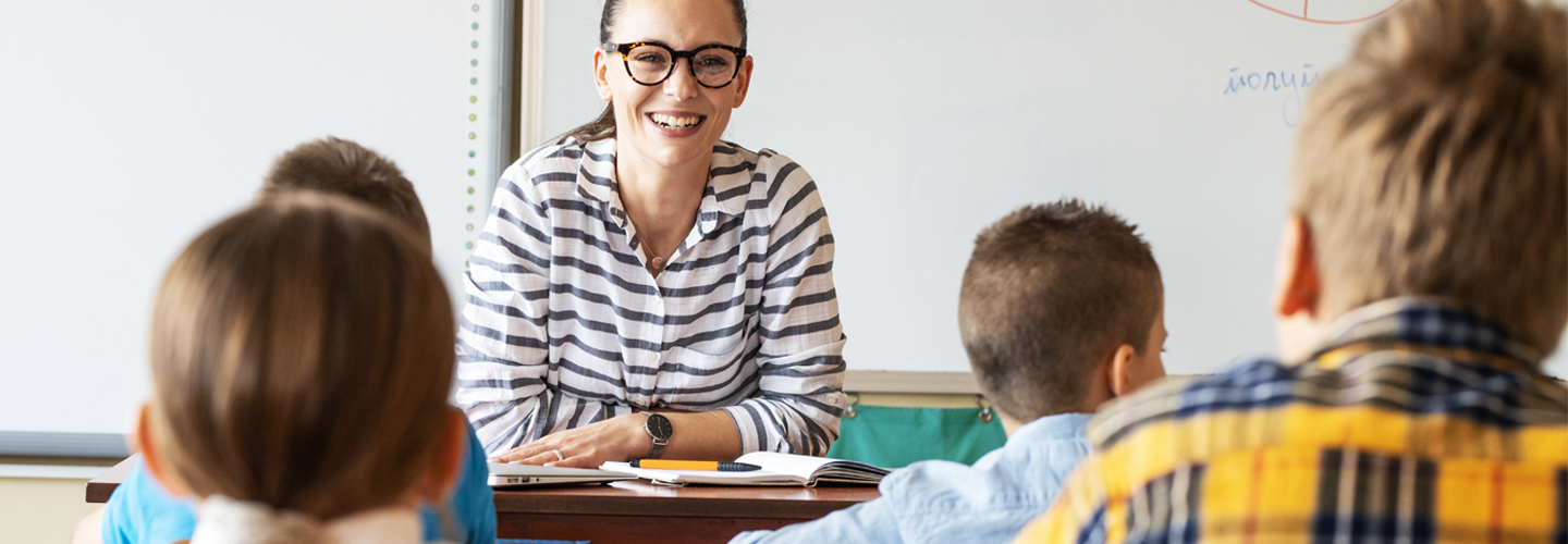 Teacher sat at a desk smiling at her students