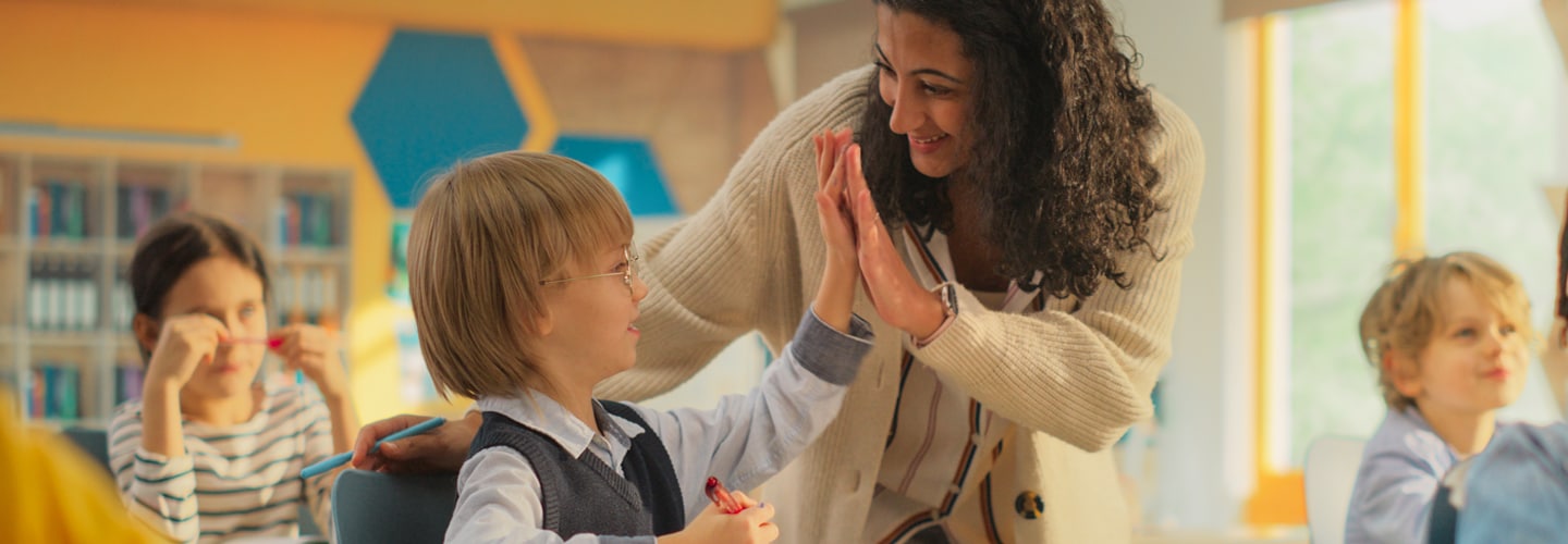 教師は若い学生の机の隣に立っていました、学生は机に座って彼の先生とハイタッチしています