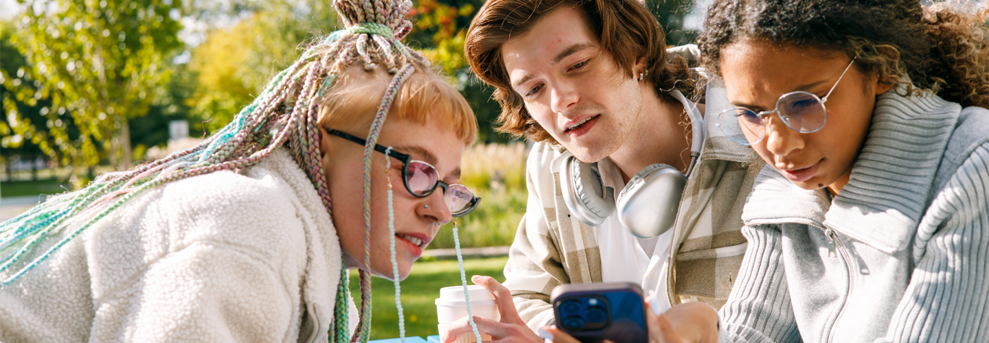 Teenage students looking at a phone together outside