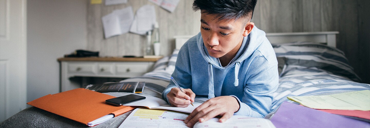 Teenager studying with open books on his bed