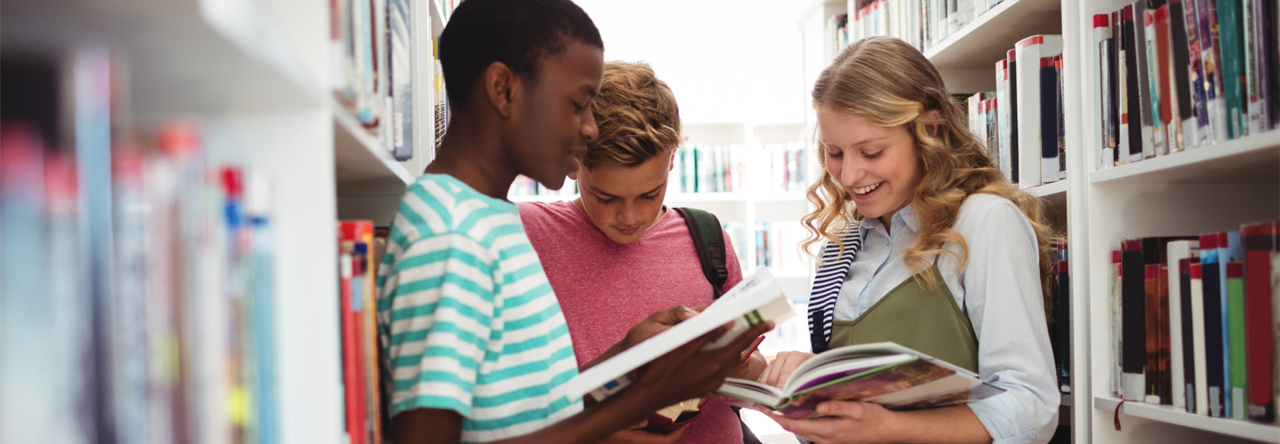 A group of teenagers reading together in a library smiling