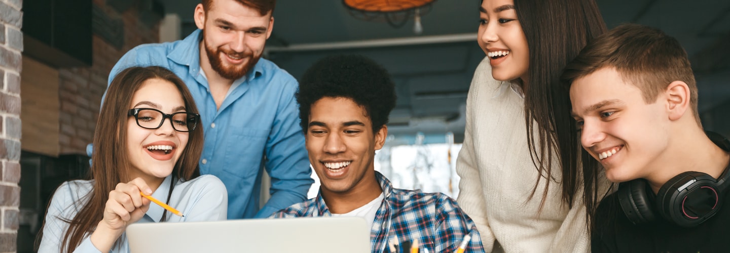 Group of four young adults collaboratively working on a laptop in a casual, modern indoor setting.