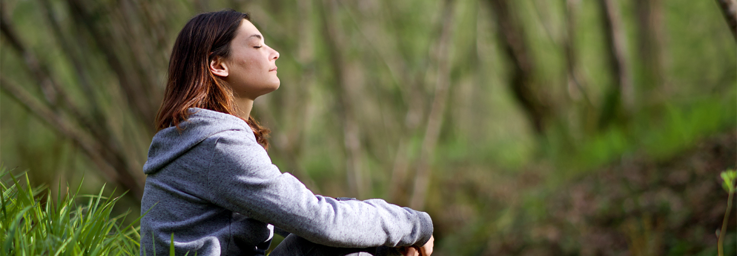 A woman sat outside in a forest relaxing with her eyes closed