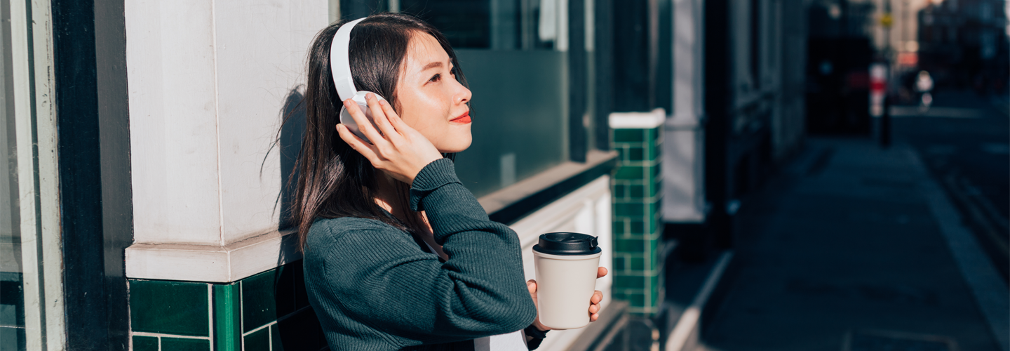 Woman standing outside with a coffee and headphones