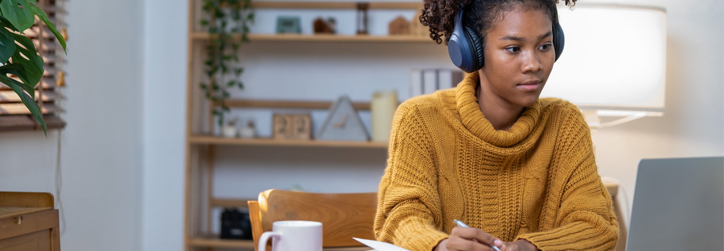 Woman with headphones on studying in front of a laptop