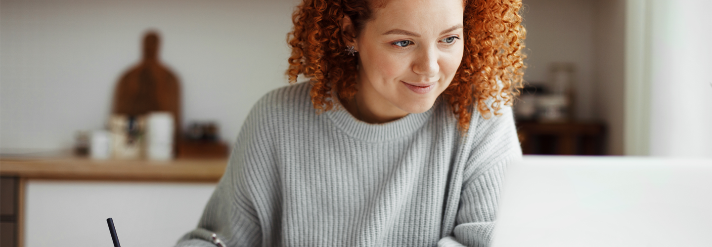 Woman working in front of a laptop writing something down and smiling