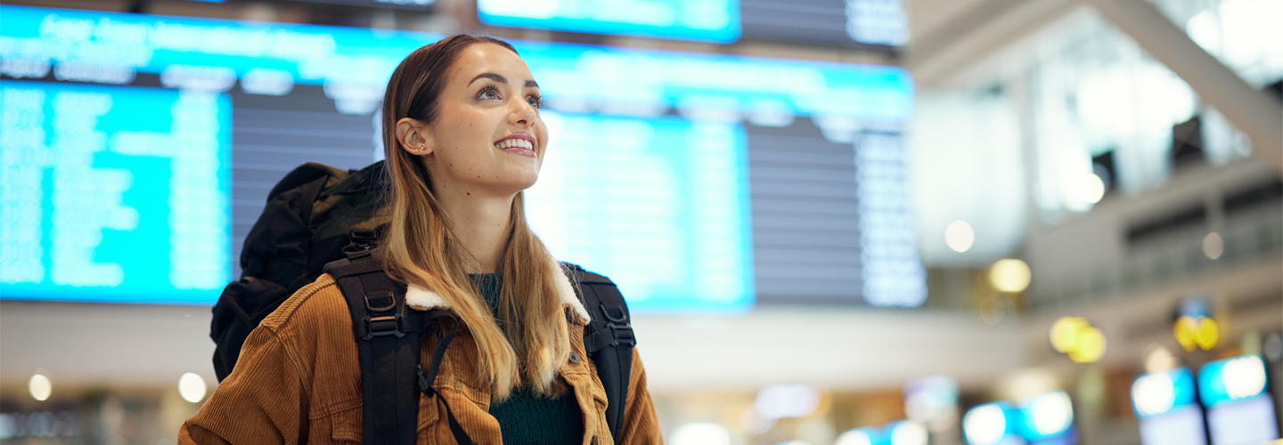 A woman with a backpack stood in a airport looking at one of the many boards