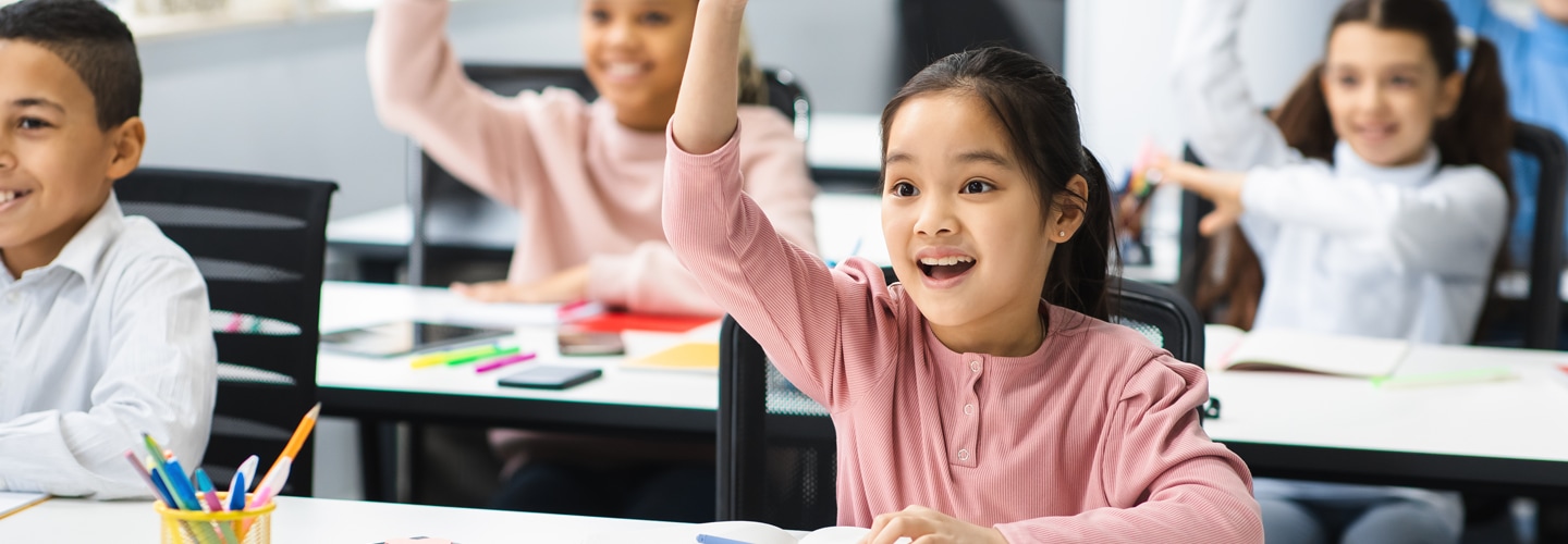 Young students in a classroom raising their hands and smiling