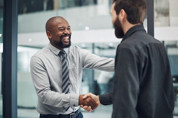 A business man smiling and shaking the hands of another man