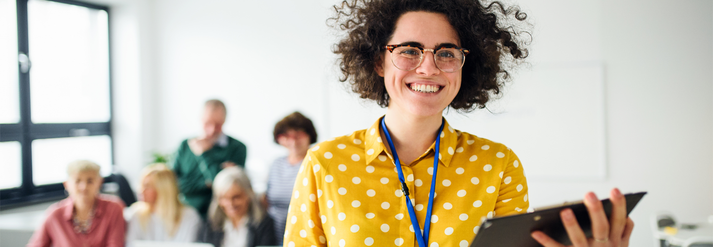 A teacher standing in front of others with a tablet smiling