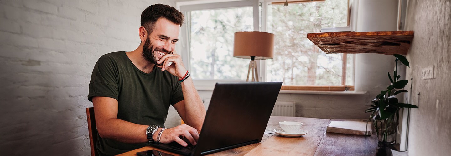 A man smiling while using his laptop at home.