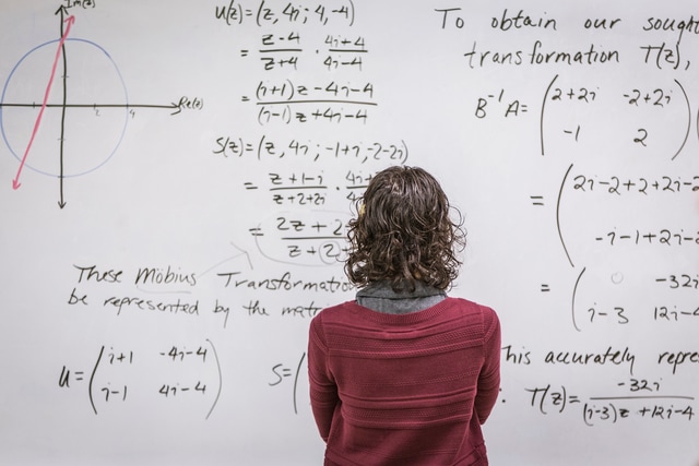 Photograph of a person looking at equations on a white board