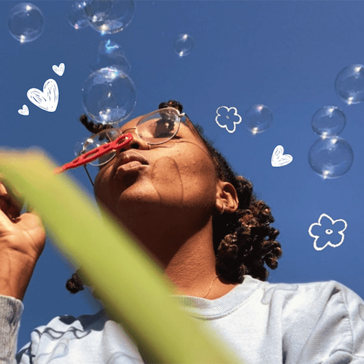 A woman with glasses blowing bubbles. There are heart and flower illustrations in the background.