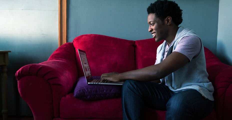 Young man on red couch using laptop.